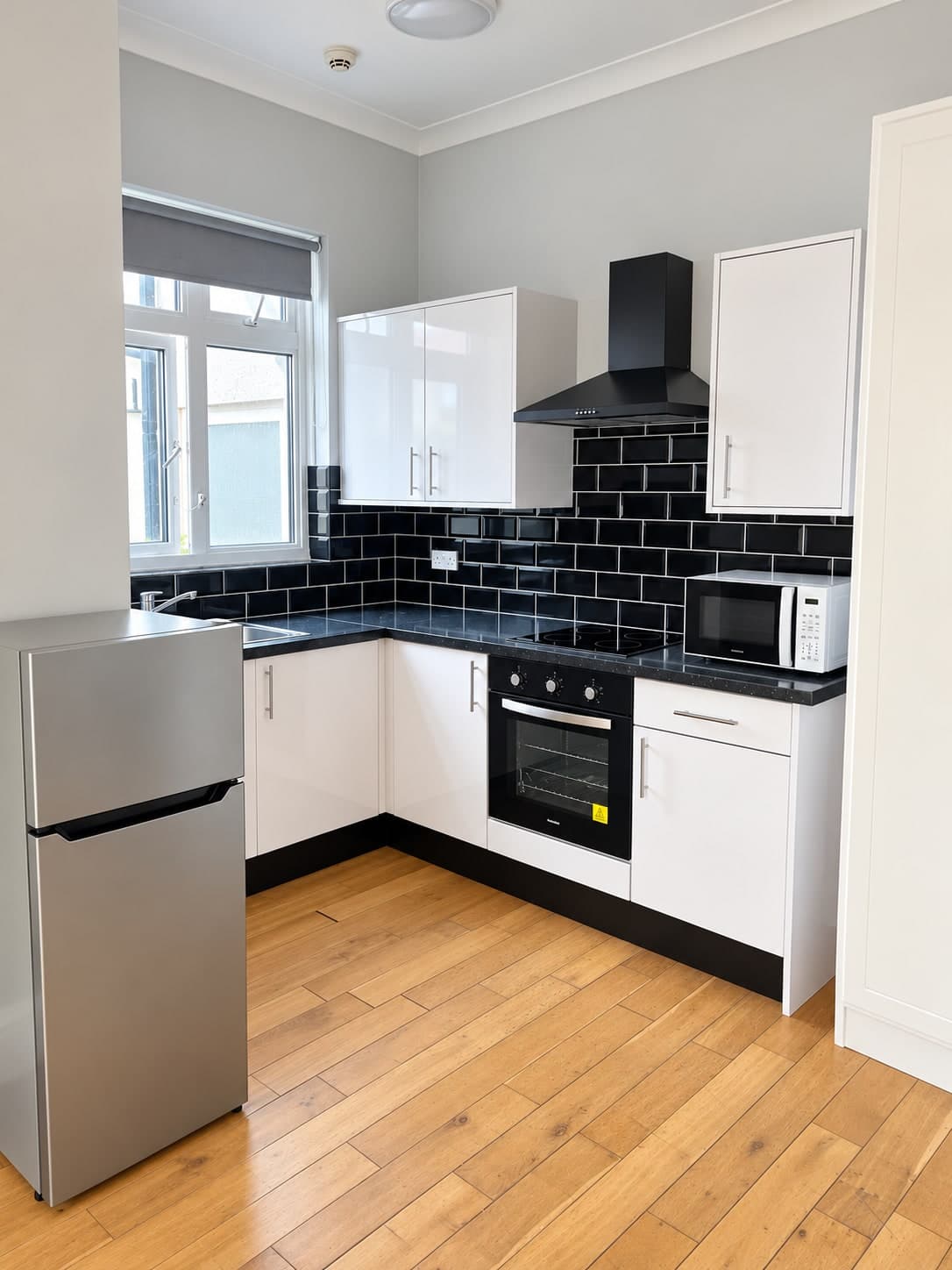 Refurbished kitchen with white cabinetry, black tiled splashback and timber flooring