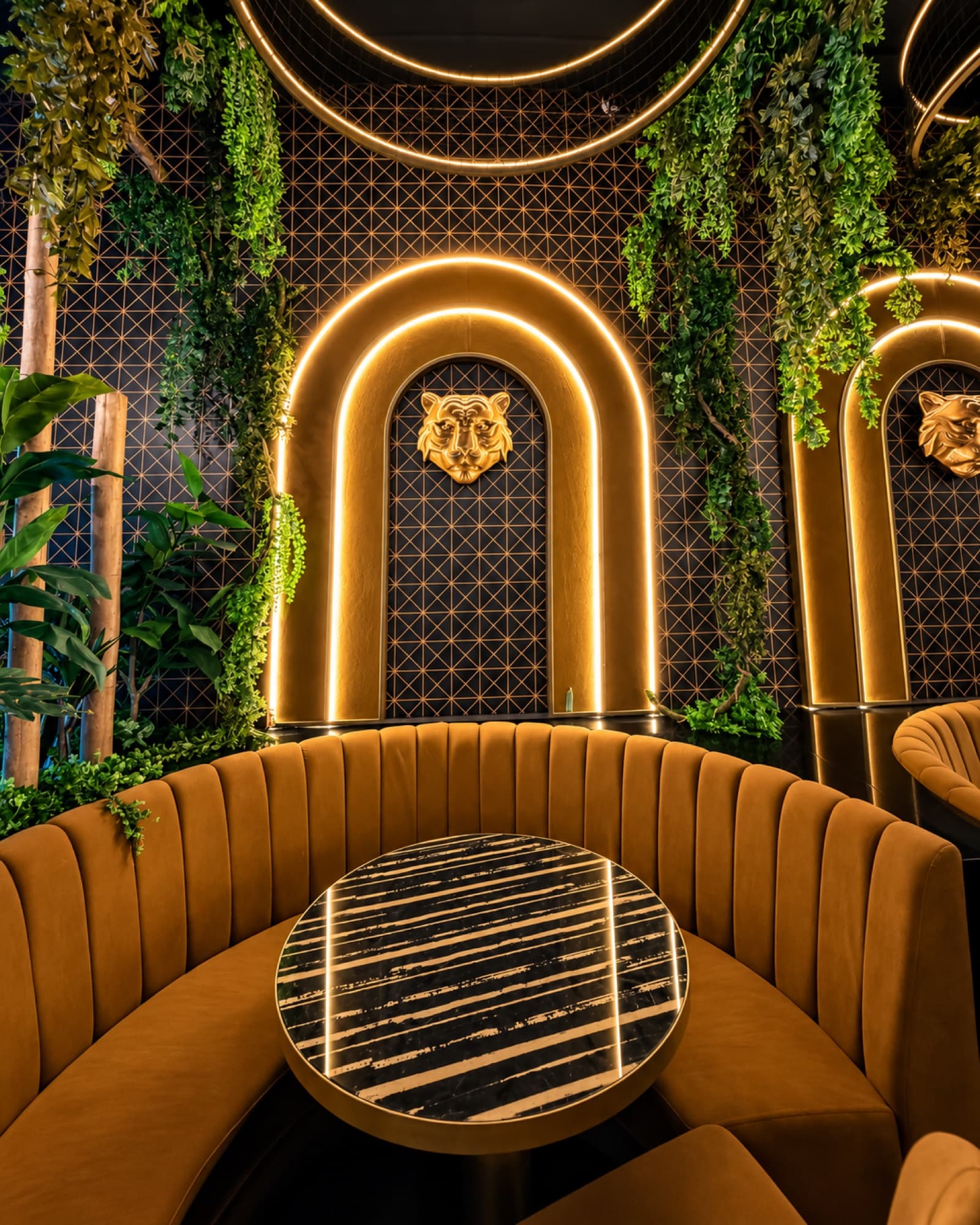 Gold-arched restaurant booth seating with tiger motif and hanging greenery