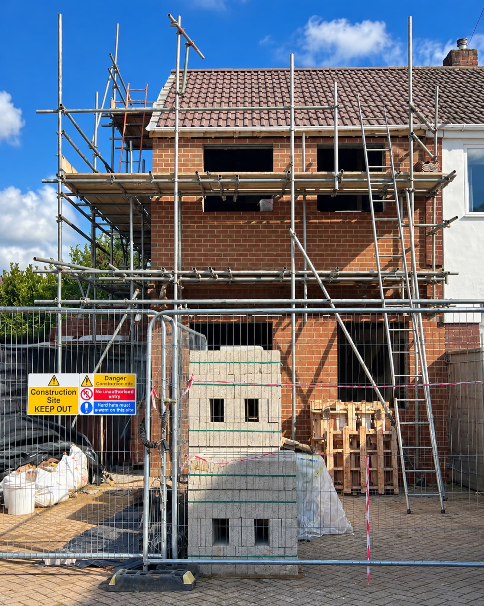 Scaffolded house under construction with blockwork stacked behind site fencing