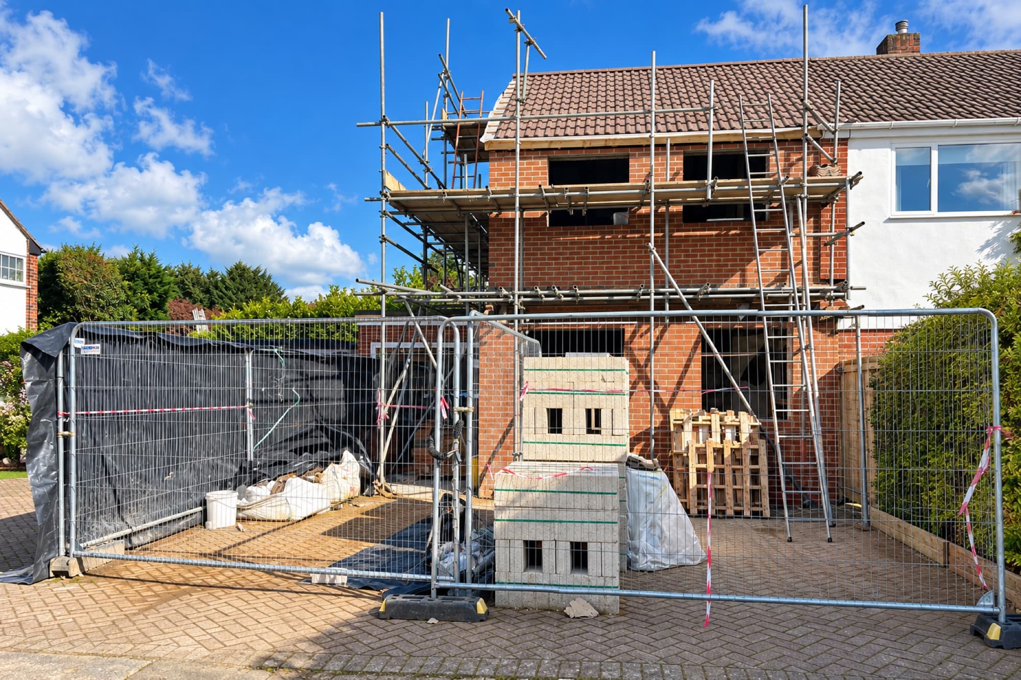 Scaffolded rear extension under construction with blockwork stacked behind site fencing