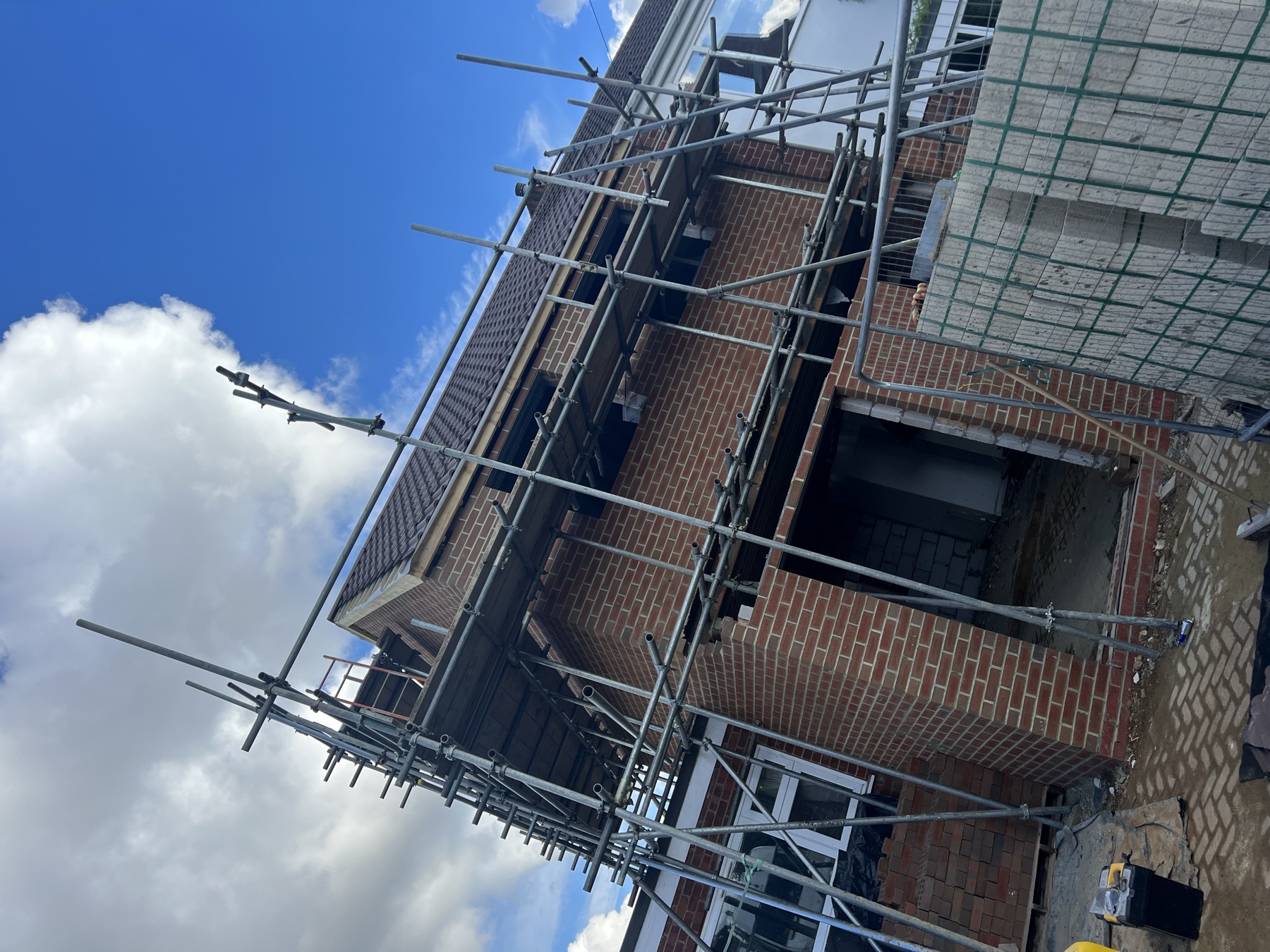 Completed first floor brickwork with window and door openings, scaffolding still up