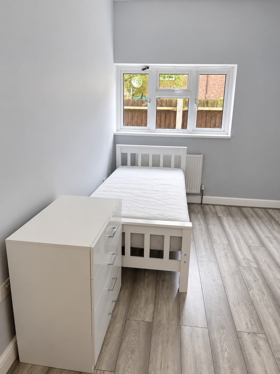 Refurbished bedroom with white furniture and grey wood-effect flooring