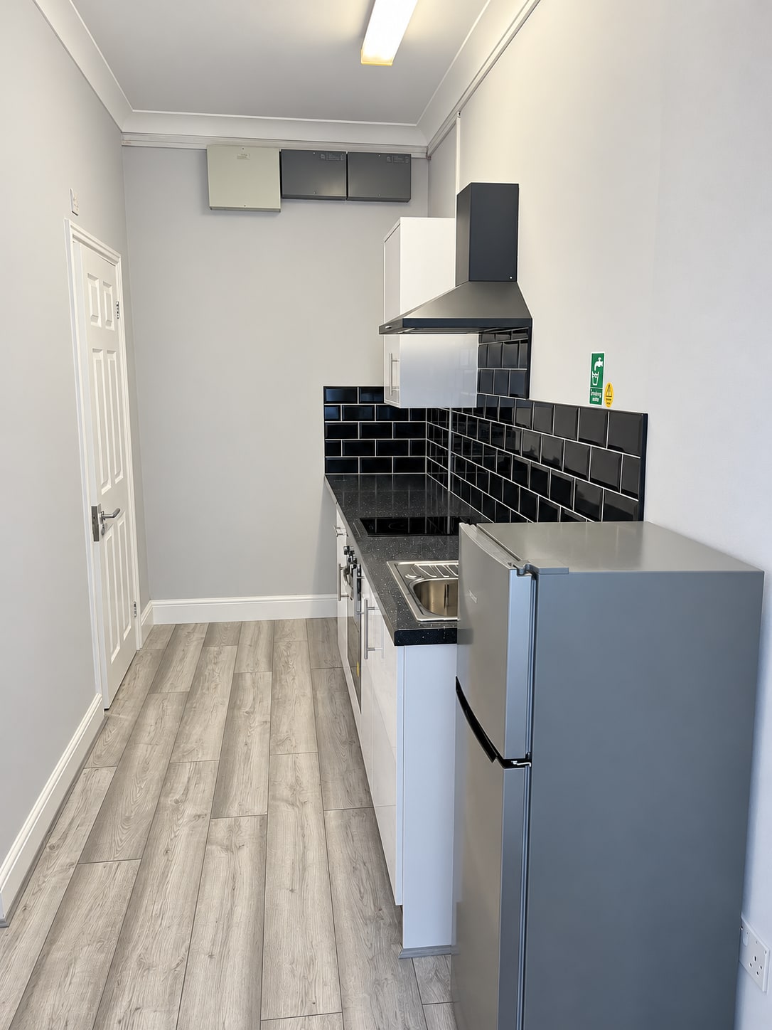 Compact kitchenette with white cabinetry, black worktop and grey flooring