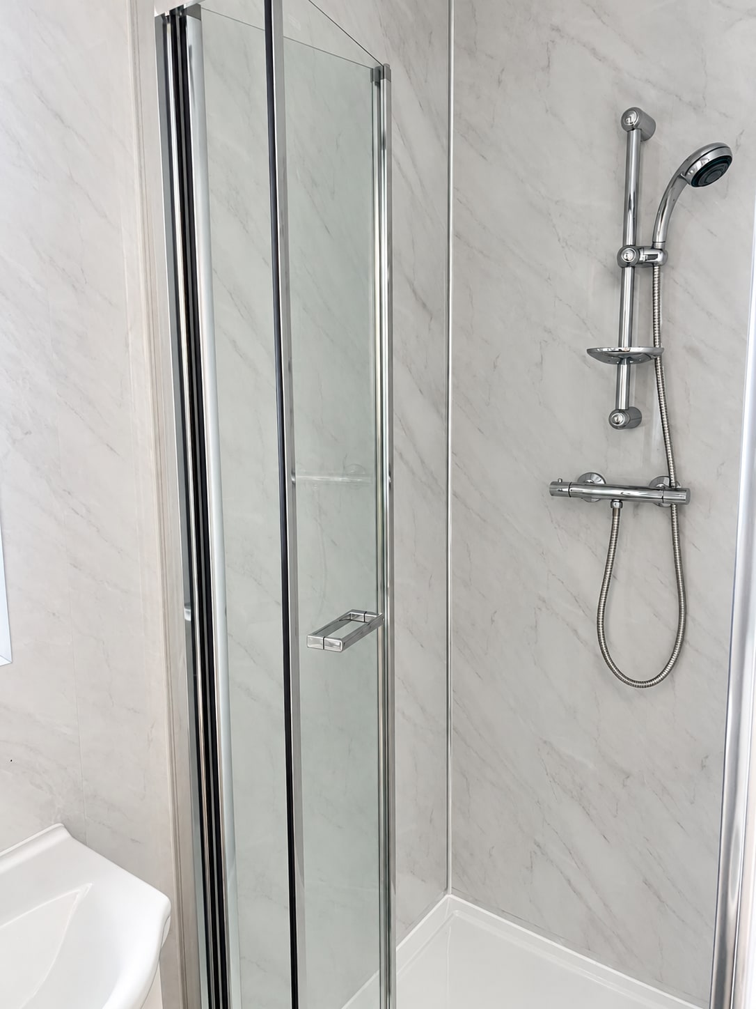 Glass shower enclosure with chrome shower fittings and marble-effect wall panels