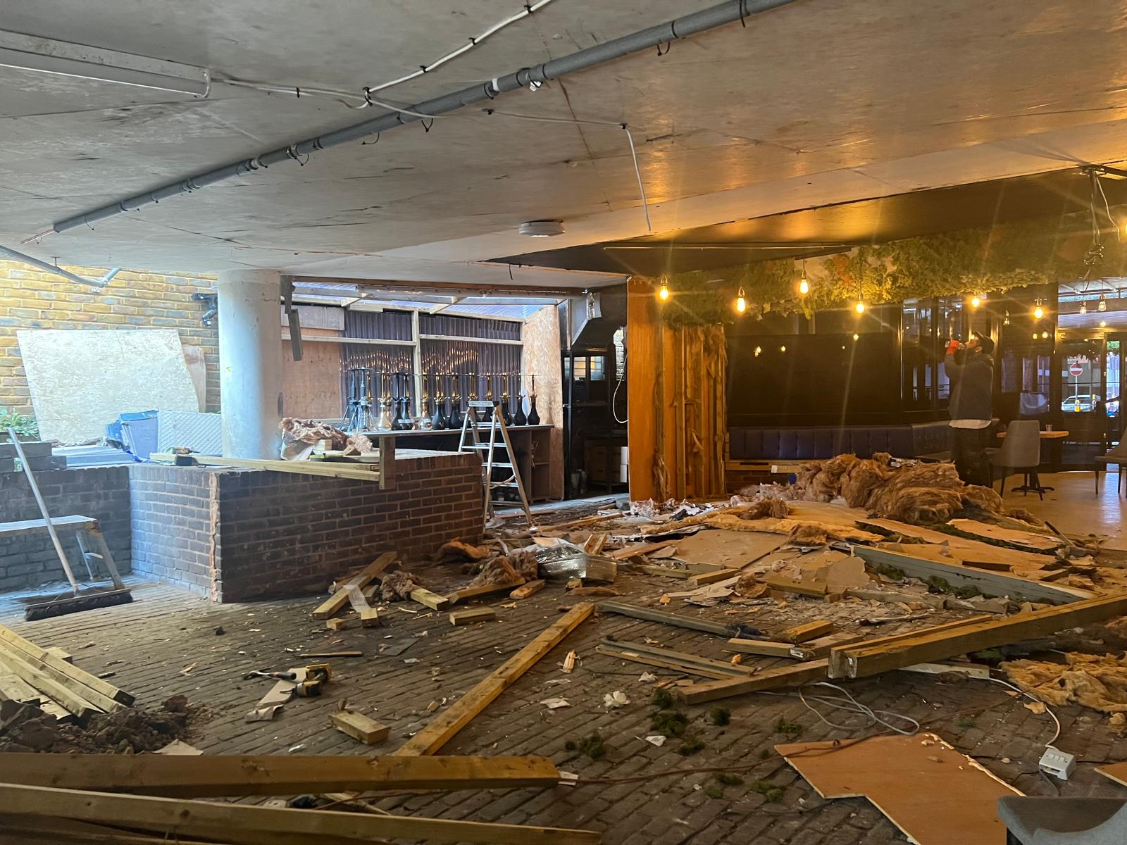 Strip-out and demolition underway, with exposed brickwork and rubble on the floor